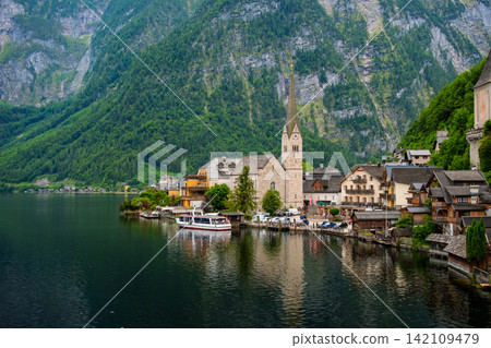 Hallstatt, Austria. A tranquil lake and a World Heritage village stretching out under a cloudy sky. Hallstatt, Austria. A tranquil lake and a World Heritage village stretching out under a cloudy sky. 142109479