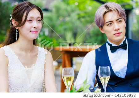 A wedding image of a bride and groom drinking champagne on a waterside terrace. A wedding image of a bride and groom drinking champagne on a waterside terrace. 142109958