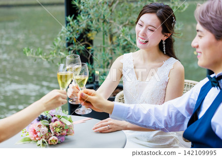 一張新郎新娘在水邊露台上喝香檳的婚禮照片。 一張新郎新娘在水邊露台上喝香檳的婚禮照片。 142109995