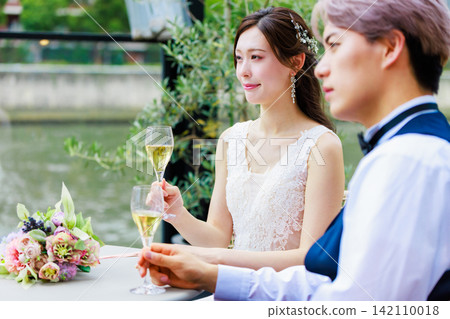 一張新郎新娘在水邊露台上喝香檳的婚禮照片。 一張新郎新娘在水邊露台上喝香檳的婚禮照片。 142110018