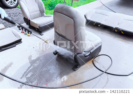 Water sprays on car seat as it is cleaned with pressure washer at home car seats are set out on driveway. Water sprays on car seat as it is cleaned with pressure washer at home car seats are set out on driveway. 142110221