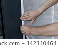 Person adjusting a mosquito screen on hook and loop tape on a frame of balcony door, illustrating home maintenance and DIY work. 142110464