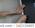 Hands securing a white mosquito screen into the window frame, illustrating precise handwork in home tasks and maintenance. 142110465