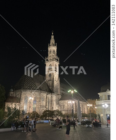 Majestic gothic cathedral tower illuminated against the dark night sky in Europe Majestic gothic cathedral tower illuminated against the dark night sky in Europe 142111083