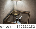 Two dropper bottles are placed on a glass-topped side table illuminated by a brass lamp. 142111132