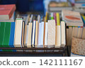 Row of assorted books standing vertically on display shelf, shallow depth of field. Pile of hardcovers and paperbacks books on table. Education, love for books, reading fiction 142111167