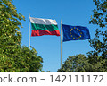 Bulgarian and European Union flags waving together against clear blue sky surrounded by green trees. National and EU flags symbolize Bulgaria, Europe, cooperation and membership 142111172