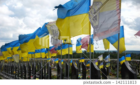 View on blue-yellow flags at countless graves of ukrainian soldiers alley of glory in Kharkiv. This site commemorates heroes and maintains the memory of wartime events in Ukraine. Slow moiton View on blue-yellow flags at countless graves of ukrainian soldiers alley of glory in Kharkiv. This site commemorates heroes and maintains the memory of wartime events in Ukraine. Slow moiton 142111813