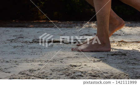 Male and female legs of pair walking on sandy beach. Bare feet of couple stepping along sand shore at sunny day. Lovers spending time together at resort. Concept of summer vacation or holiday Male and female legs of pair walking on sandy beach. Bare feet of couple stepping along sand shore at sunny day. Lovers spending time together at resort. Concept of summer vacation or holiday 142111999
