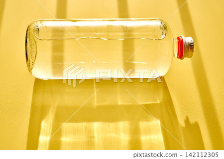 Glass bottle with water on yellow background casting shadows Glass bottle with water on yellow background casting shadows 142112305