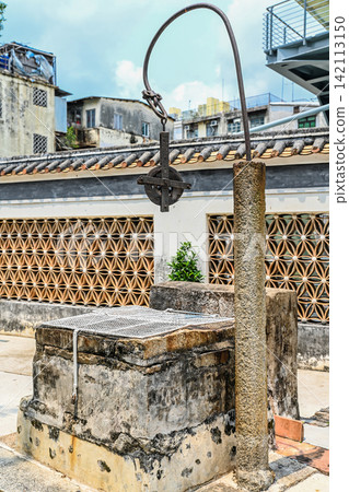 Ancient stone water well with iron pulley in Mandarin House with modern buildings background Ancient stone water well with iron pulley in Mandarin House with modern buildings background 142113150