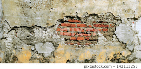 A cracked concrete wall with peeling paint and exposed red brick. A cracked concrete wall with peeling paint and exposed red brick. 142113253