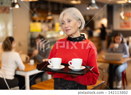 Breakfast in cafe - mature woman carries tray with two cups of coffee Breakfast in cafe - mature woman carries tray with two cups of coffee 142113802