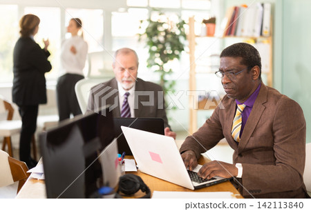 Businessmen use laptops during a conference in meeting room with colleagues Businessmen use laptops during a conference in meeting room with colleagues 142113840