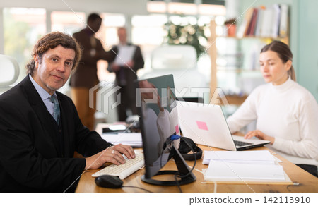 Businessman works in company office along with other office workers 142113910