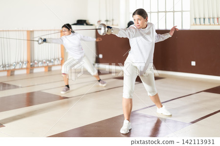 Young woman practicing epee exercises in sports hall Young woman practicing epee exercises in sports hall 142113931