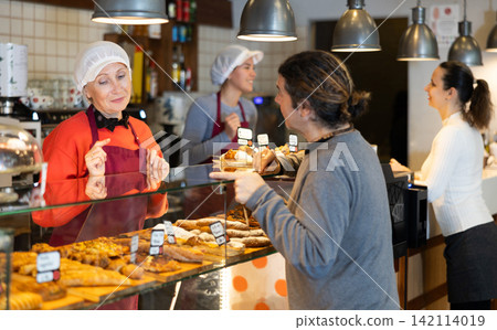 Bakery shop senior female assistant talk to customer, answers questions and recommends fresh products Bakery shop senior female assistant talk to customer, answers questions and recommends fresh products 142114019