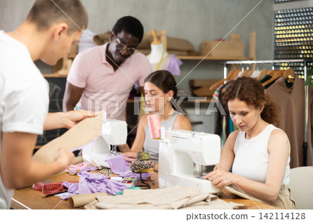 Smiling woman stitching fabric on machine in sewing class for adults Smiling woman stitching fabric on machine in sewing class for adults 142114128