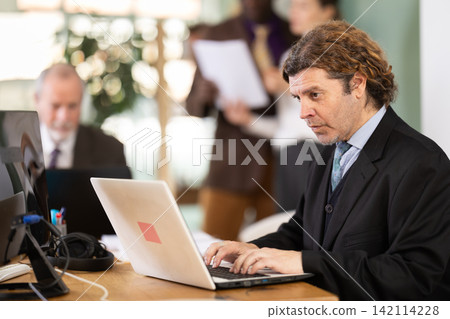 Man sitting at desk is working on laptop computer. Working day in office Man sitting at desk is working on laptop computer. Working day in office 142114228