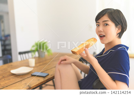 A woman in pajamas eating toast for breakfast. A woman in pajamas eating toast for breakfast. 142114254
