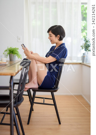 一位女士坐在椅子上看著她的智慧型手機。 一位女士坐在椅子上看著她的智慧型手機。 142114261