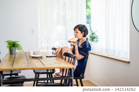 一位年輕女子在吃早餐時查看智慧型手機。 一位年輕女子在吃早餐時查看智慧型手機。 142114262