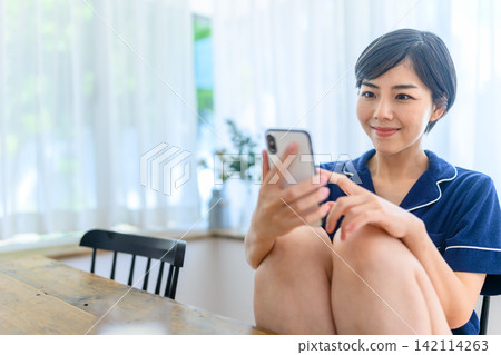 一位身穿家居服的女士正在看著她的智慧型手機。 一位身穿家居服的女士正在看著她的智慧型手機。 142114263