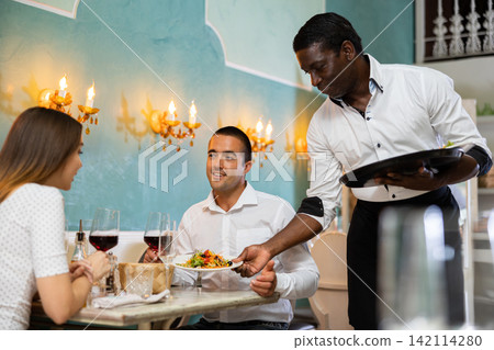 Waiter brings meals for a couple Waiter brings meals for a couple 142114280