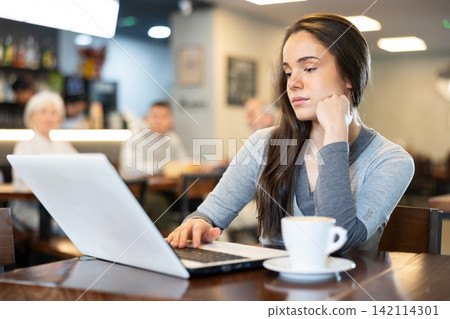 Girl works on a laptop and drinks coffee in cafe interior 142114301