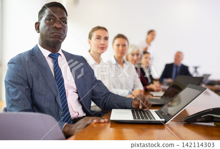 Mature african businessman sitting at meeting and listening to colleague's report Mature african businessman sitting at meeting and listening to colleague's report 142114303