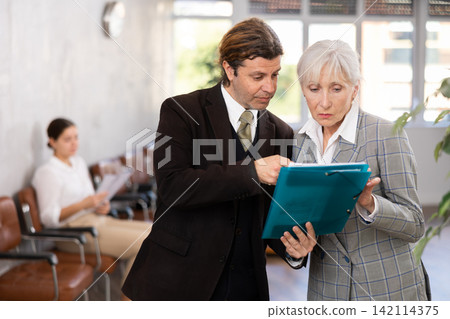 Man discussing working documents with senior female colleague Man discussing working documents with senior female colleague 142114375