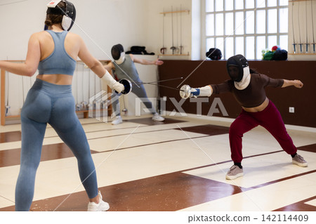 women in protective masks are conducting a fencing training women in protective masks are conducting a fencing training 142114409