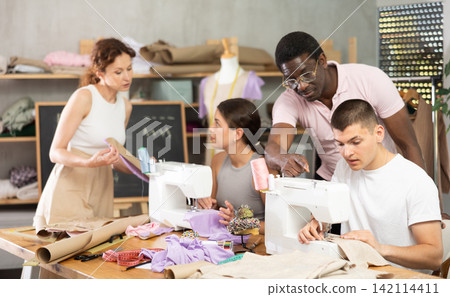 Sewing teacher helping student with machine threading in workshop 142114411