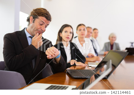 Businessman looking at wristwatch at business meeting in meeting room Businessman looking at wristwatch at business meeting in meeting room 142114461