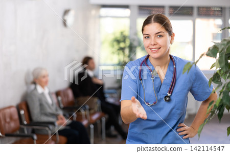 Cheerful woman physician standing in office, looking at camera and gesturing Cheerful woman physician standing in office, looking at camera and gesturing 142114547