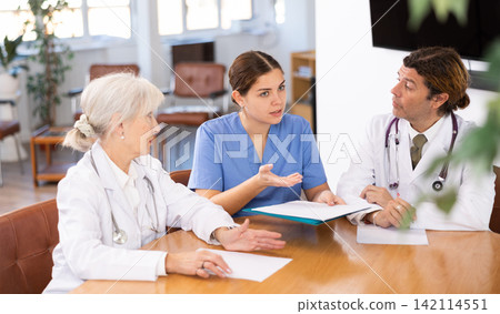 three positive doctors are sitting at table animatedly and actively discussing current work three positive doctors are sitting at table animatedly and actively discussing current work 142114551