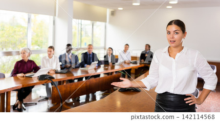 Confident young woman manager making presenting gesture in conference room Confident young woman manager making presenting gesture in conference room 142114568