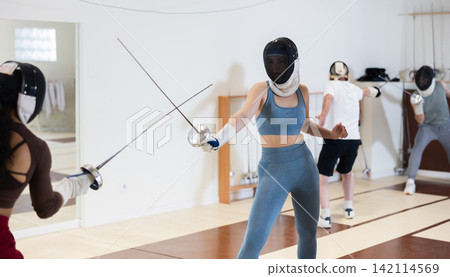 women in protective masks are conducting a fencing training women in protective masks are conducting a fencing training 142114569