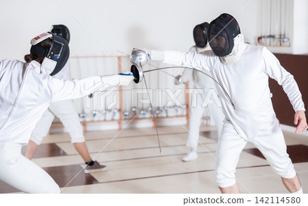Man and woman fencing sparring during training in gym Man and woman fencing sparring during training in gym 142114580