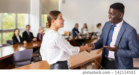 Middle aged african male manager welcoming a new white female employee Middle aged african male manager welcoming a new white female employee 142114581