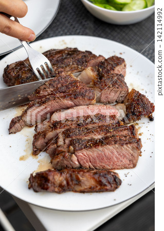 Slicing Freshly Grilled Beef Steak on Plate on Garden Terrace Table Slicing Freshly Grilled Beef Steak on Plate on Garden Terrace Table 142114992
