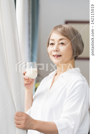 一位老婦人在客廳窗邊喝牛奶。 一位老婦人在客廳窗邊喝牛奶。 142115019