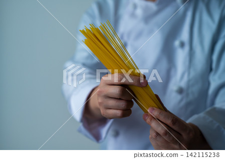 廚師正在炫耀他手裡拿著的乾意麵。 廚師正在炫耀他手裡拿著的乾意麵。 142115238