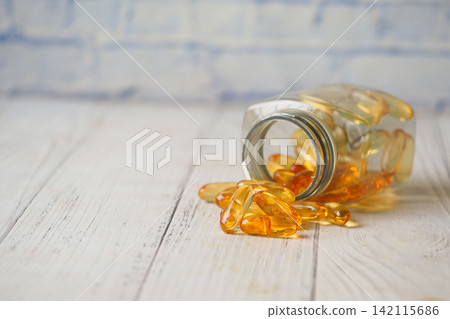 Spilled bottle of fish oil capsules on wooden surface 142115686