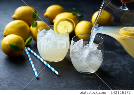 Lemonade with fresh lemon in glasses on dark background. Cold refreshing lemonade for summer party and fun. Lemonade with fresh lemon in glasses on dark background. Cold refreshing lemonade for summer party and fun. 142116172
