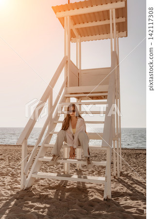 Beach lifeguard tower woman sitting on the steps on a sunny day with ocean background Beach lifeguard tower woman sitting on the steps on a sunny day with ocean background 142117308