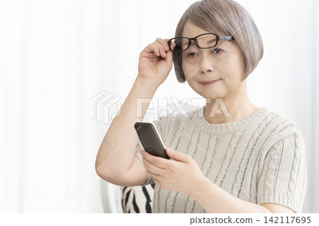 一位戴著老花眼鏡的老婦人在客廳打電話。 一位戴著老花眼鏡的老婦人在客廳打電話。 142117695