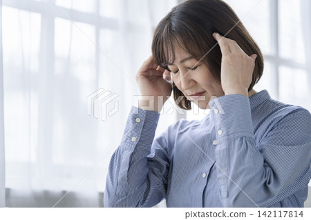 A woman in her late 40s holding her temples. A woman in her late 40s holding her temples. 142117814