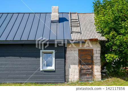 Old House With Renovated Metal Roof and Weathered Extension Under Blue Sky Old House With Renovated Metal Roof and Weathered Extension Under Blue Sky 142117856