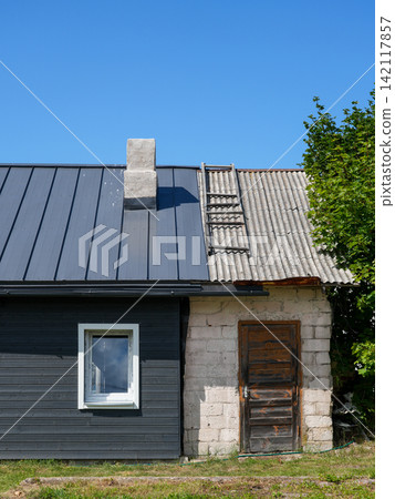 Old Rural House With Renovated Metal Roof and Weathered Corrugated Roofing Section Old Rural House With Renovated Metal Roof and Weathered Corrugated Roofing Section 142117857